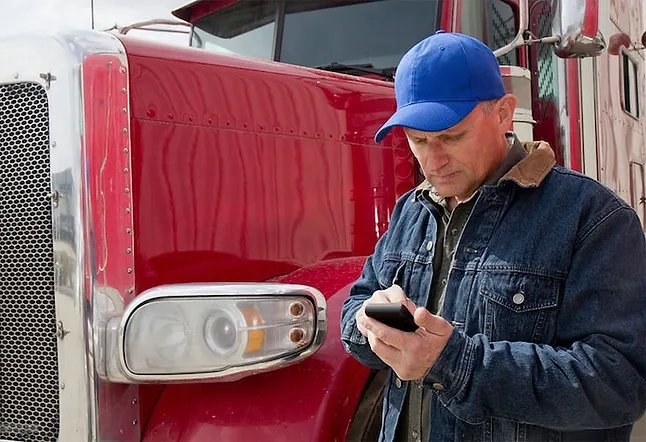 Carrier trucker next to his semi using his phone.