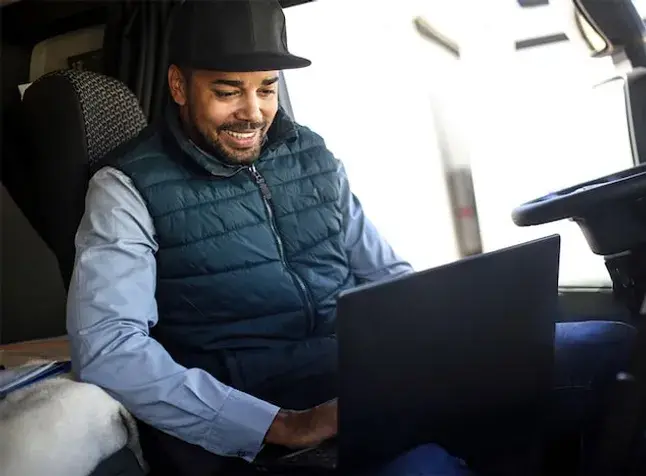 Happy driver in his stationary hauler using his laptop computer.